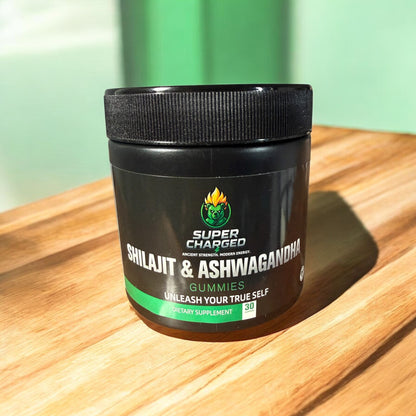 Supplement jar labeled 'Super Charged Shilajit & Ashwagandha Gummies' on a wooden surface with a green background.