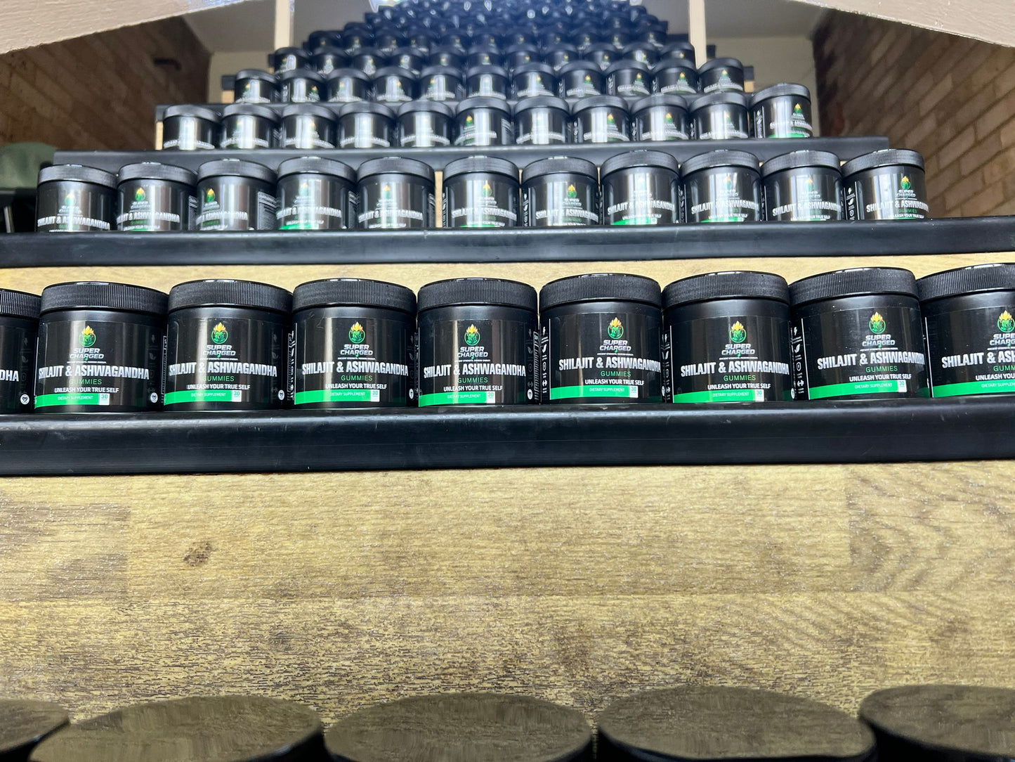 Multiple black containers with green labels on a wooden shelf.